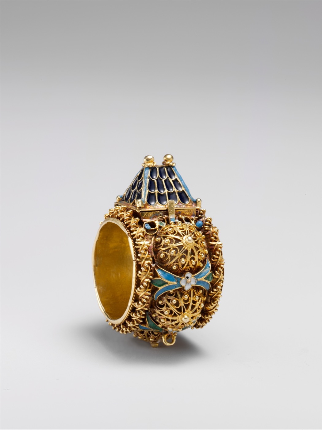 A gold Jewish ceremonial wedding ring topped with a tiny house with a blue enamel roof