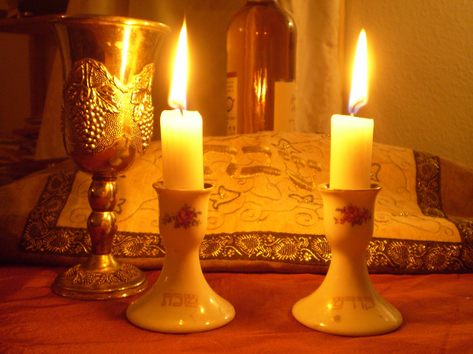 Two lit Shabbat candles, a kiddush cup, and the covered challah, set for Friday evening